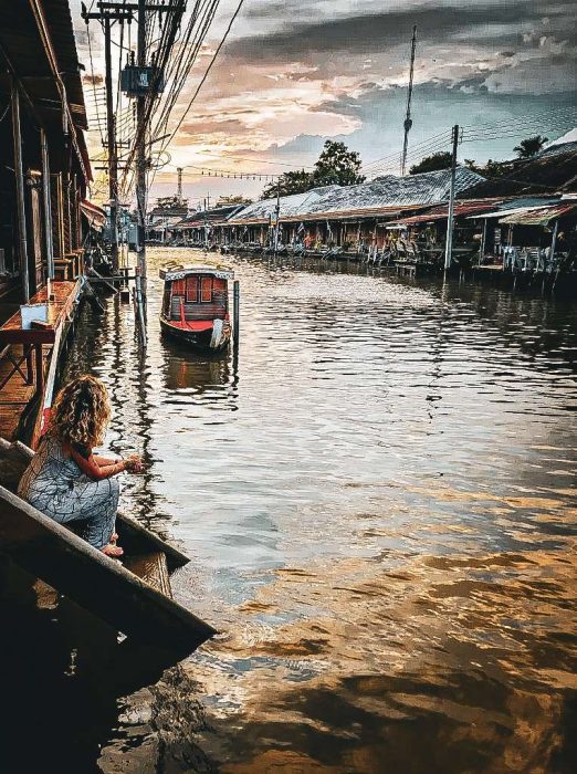 bateau et femme assise sur des marches au bord de l'eau a amphawa 