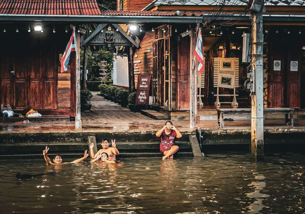 groupe d'enfant en train de se baigner et saluer dans un klong d'amphawa en thailande