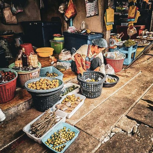 vendeuse du marche de mae klong assise au mileu de ses paniers de fruits