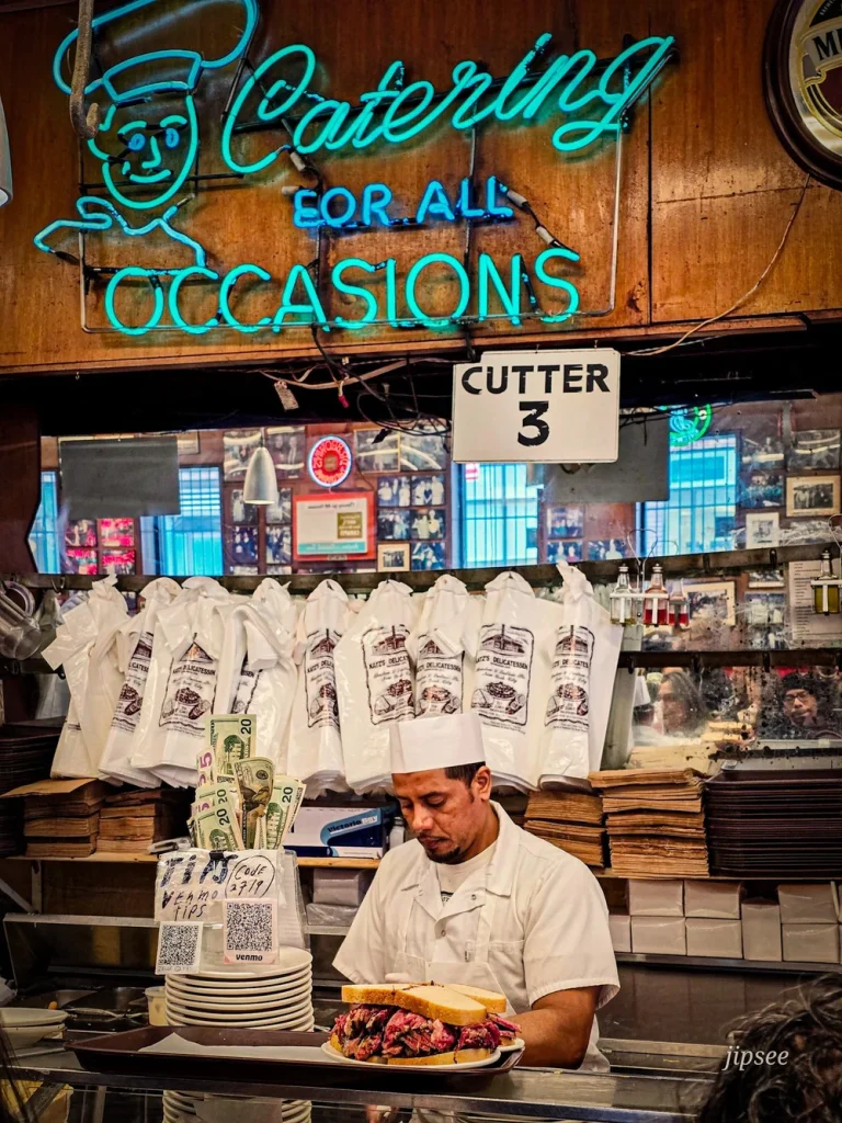 venseur de sandwich au pastrami devant son comptoir avec sacs et enseigne lumineuse 