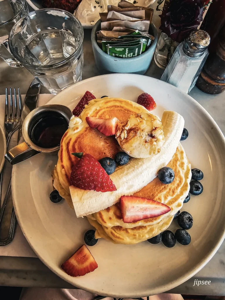 pancakes sucrés banane fraise sirop d'erable myrtille servis dans une assiette blanche