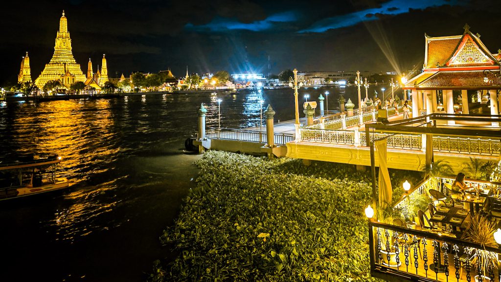temple wat arun illuminé vu d'une terrasse de restaurant de l'autre cote du fleuve de bangkok