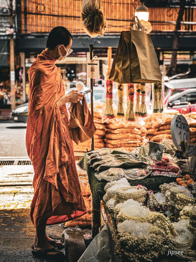 moine thailandais en tenue traditionnel devant un étal au marché aux fleurs de bangkok