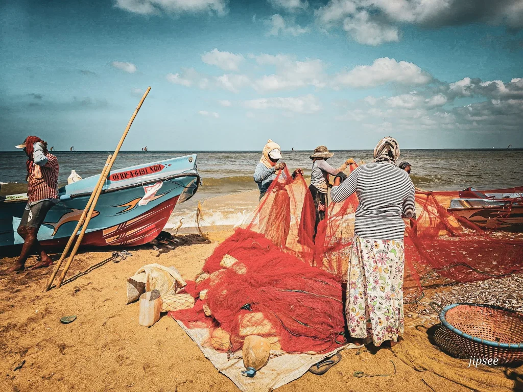 femme triant des filets de peche sur la plage pecheur adossé a son bateau sur la plage de negombo
