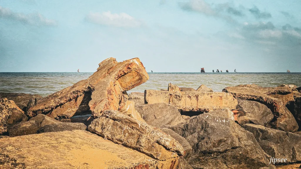 rocher en forme de croix sur la plage bateaux a voile au loin voguant dans l'ocean indien