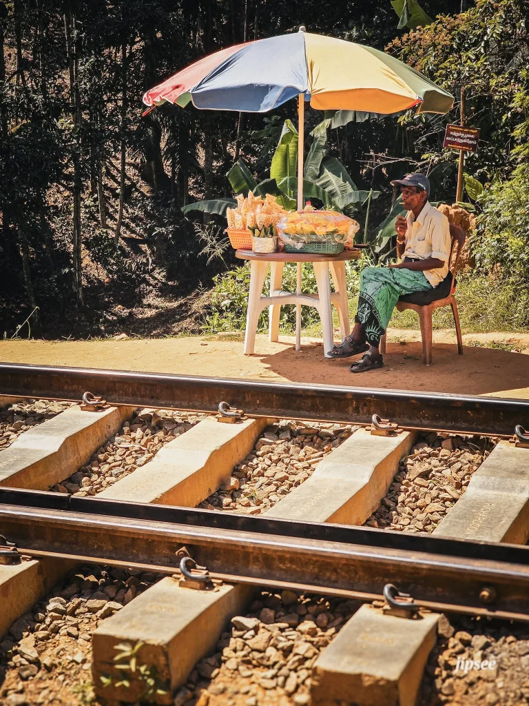 homme fumant une cigarette devant des rail assis a coté d'un stand sous un parasol
