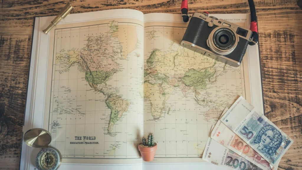 livre ouvert sur une illustation de carte du monde billets de banque et appareil photo etalés autour