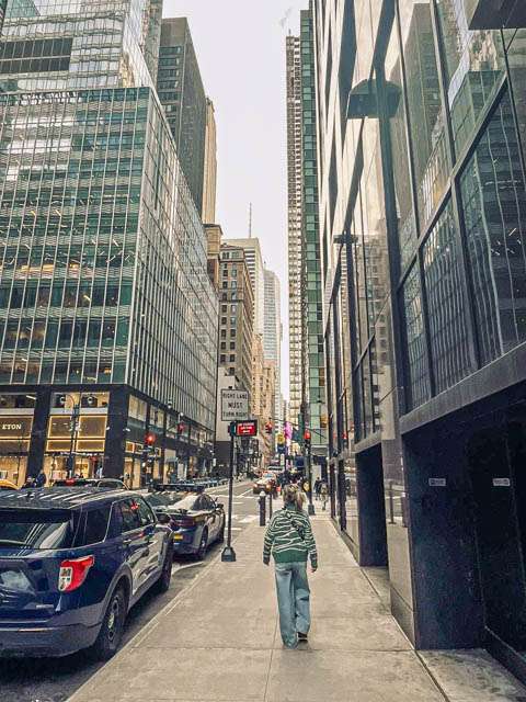 femme de dos marchant dans une rue entourée de buildings