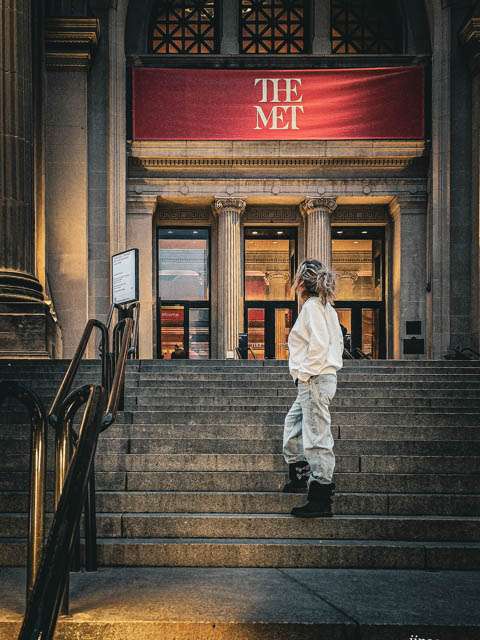 femme de dos sur les marches du met new york regardant l'enseigne rouge du musée