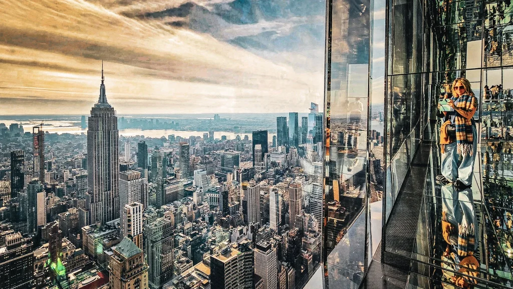 femme prenant une photo derriere une baie vitrée decouvrant les gratte ciel new yorkais