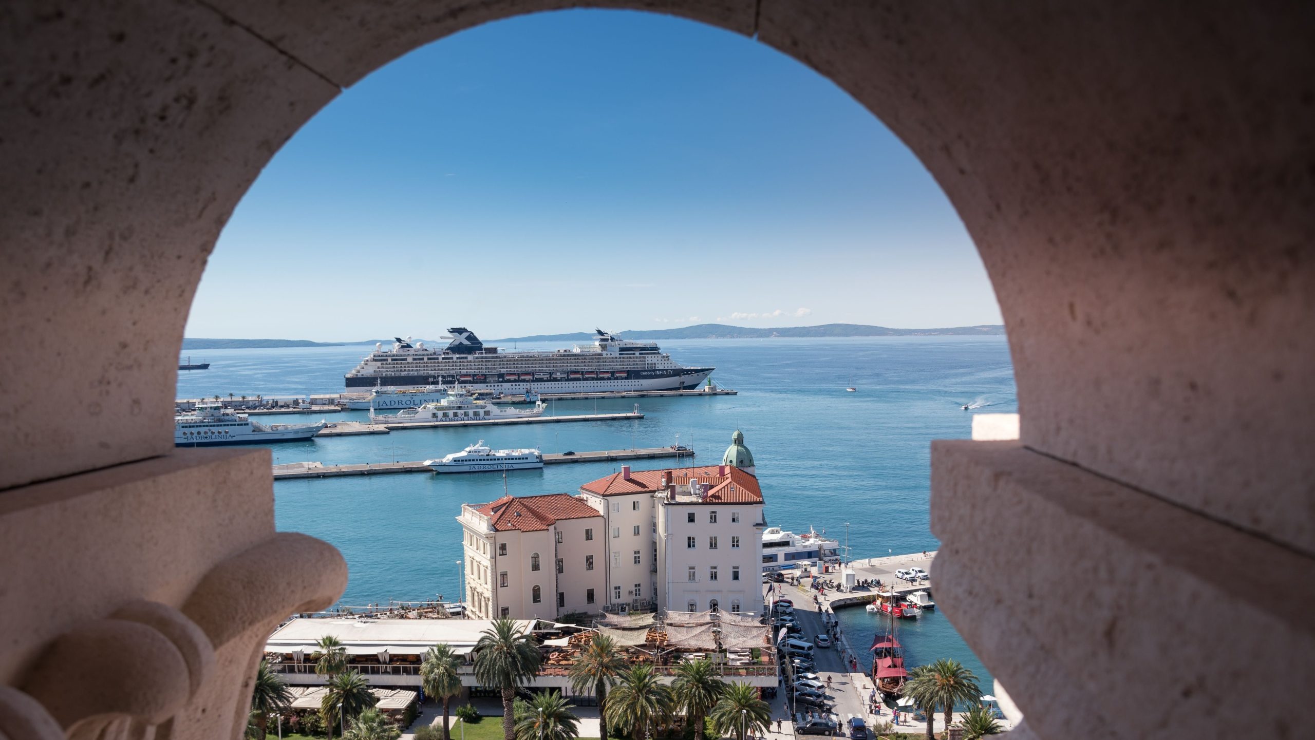 View of a cruise ship in Split, Croatia from an arched stone window, showcasing summer sea beauty.