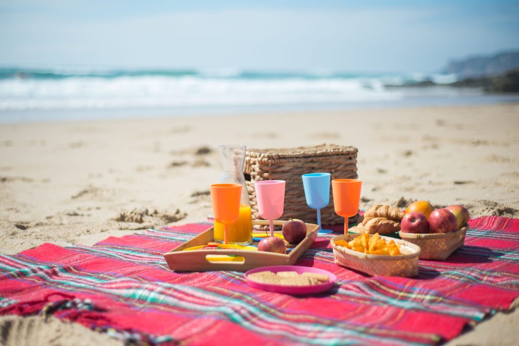 Enjoy a vibrant beach picnic scene with colorful cups and fresh fruits on the sandy shores of Portugal.