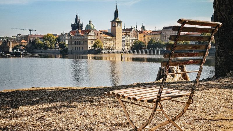 chaise en bois en bord de fleuve et vue du centre ville de prague en fond