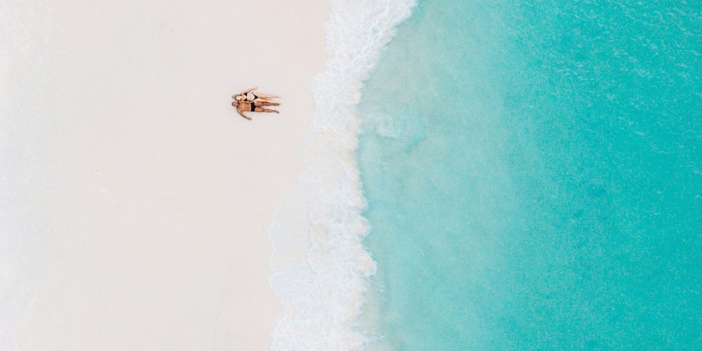 couple allongés cote a cote sur une plage deserte vue de drone