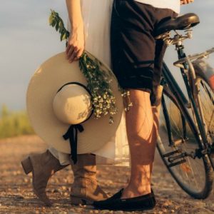 jambe de couple enlacés devant un vélo la femme tient un chapeau et un bouquet de fleurs