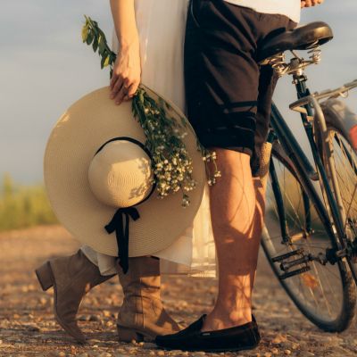 jambe de couple enlacés devant un vélo la femme tient un chapeau et un bouquet de fleurs