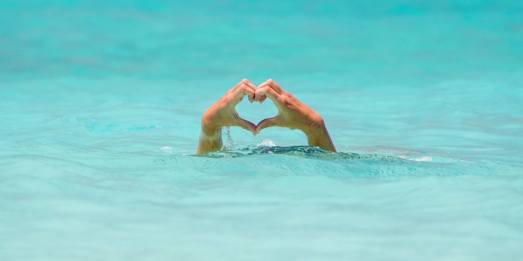 mains sortant d'une eau turquoise formant un coeur avec des doigts