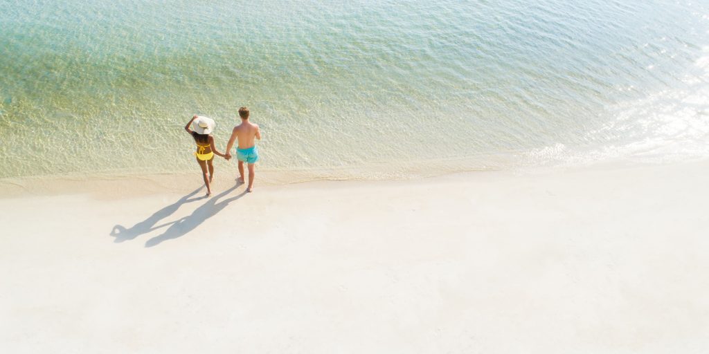 couple partant se baigner main dans la main seuls sur une plage