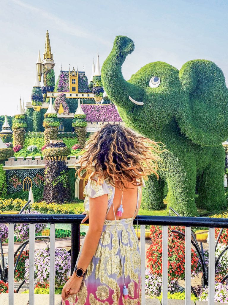 pose photo d'une femme de dos devant un chateau et un elephant couvert de vegetation au dubai miracle garden