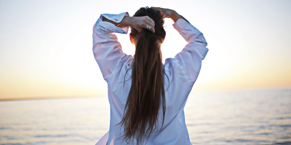 femme brune s'attachant les cheveux de dos sur une plage