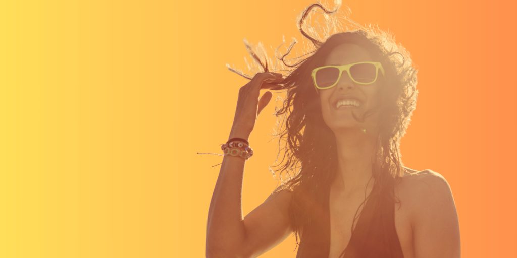 femme souriante avec cheveux au vent et lunette de soleil