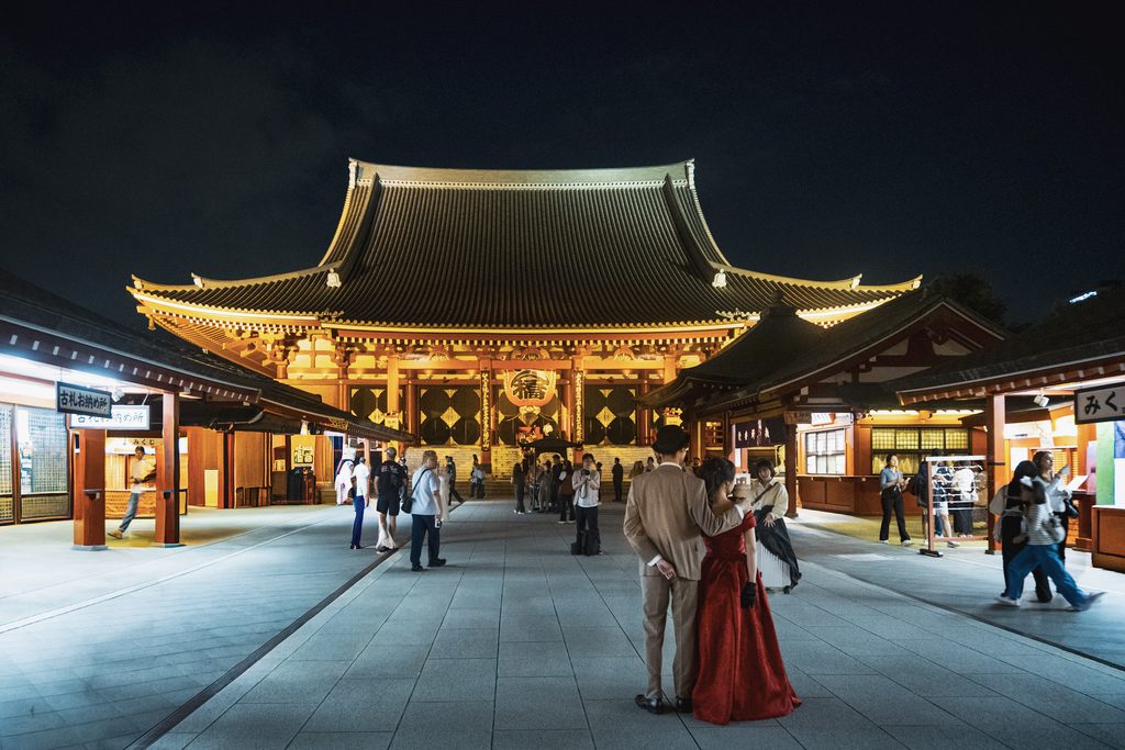 entree du temple senso ji la nuit a tokyo avec un couple posant pour un photographe devant